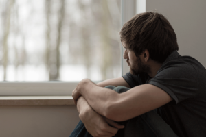 Man looking out window and thinking about addiction and mental health